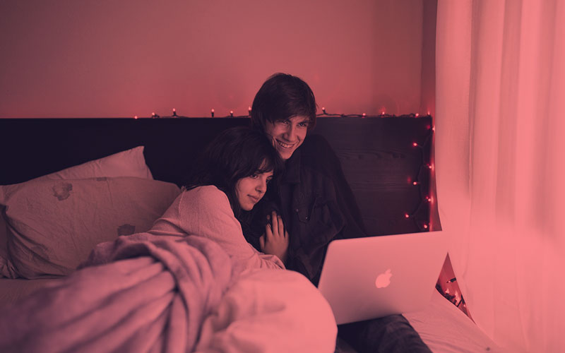A couple sitting on a bed using a laptop