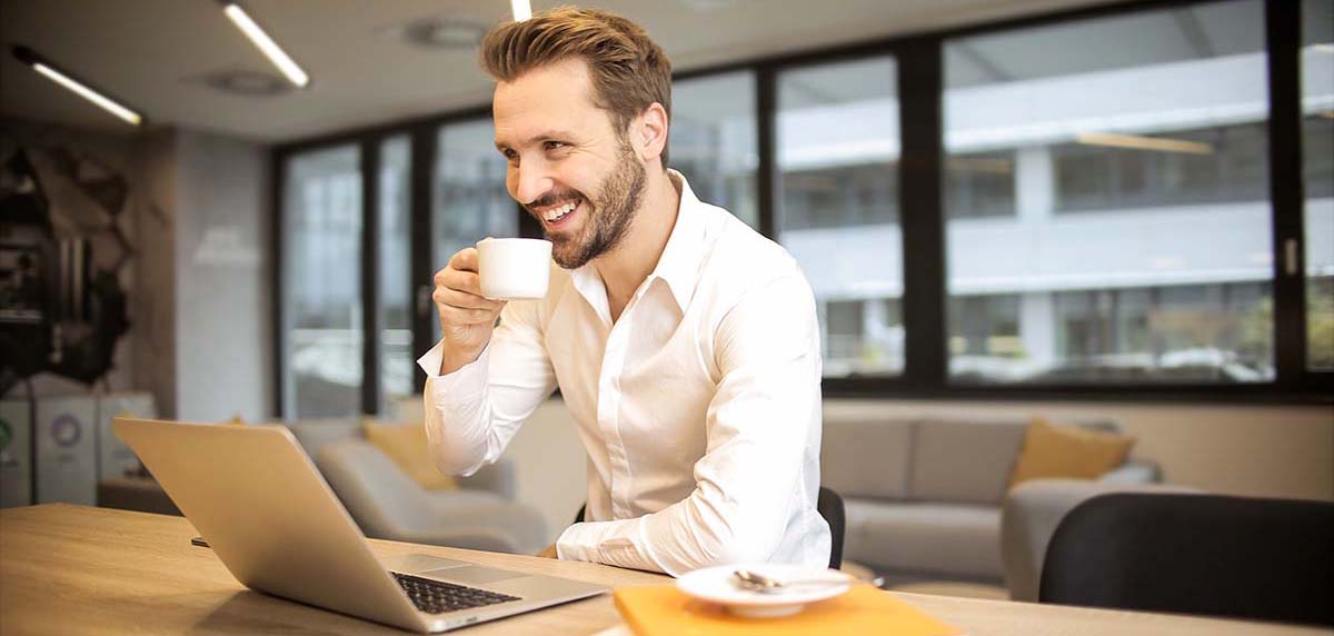 Man smiling drinking coffee in front of laptop
